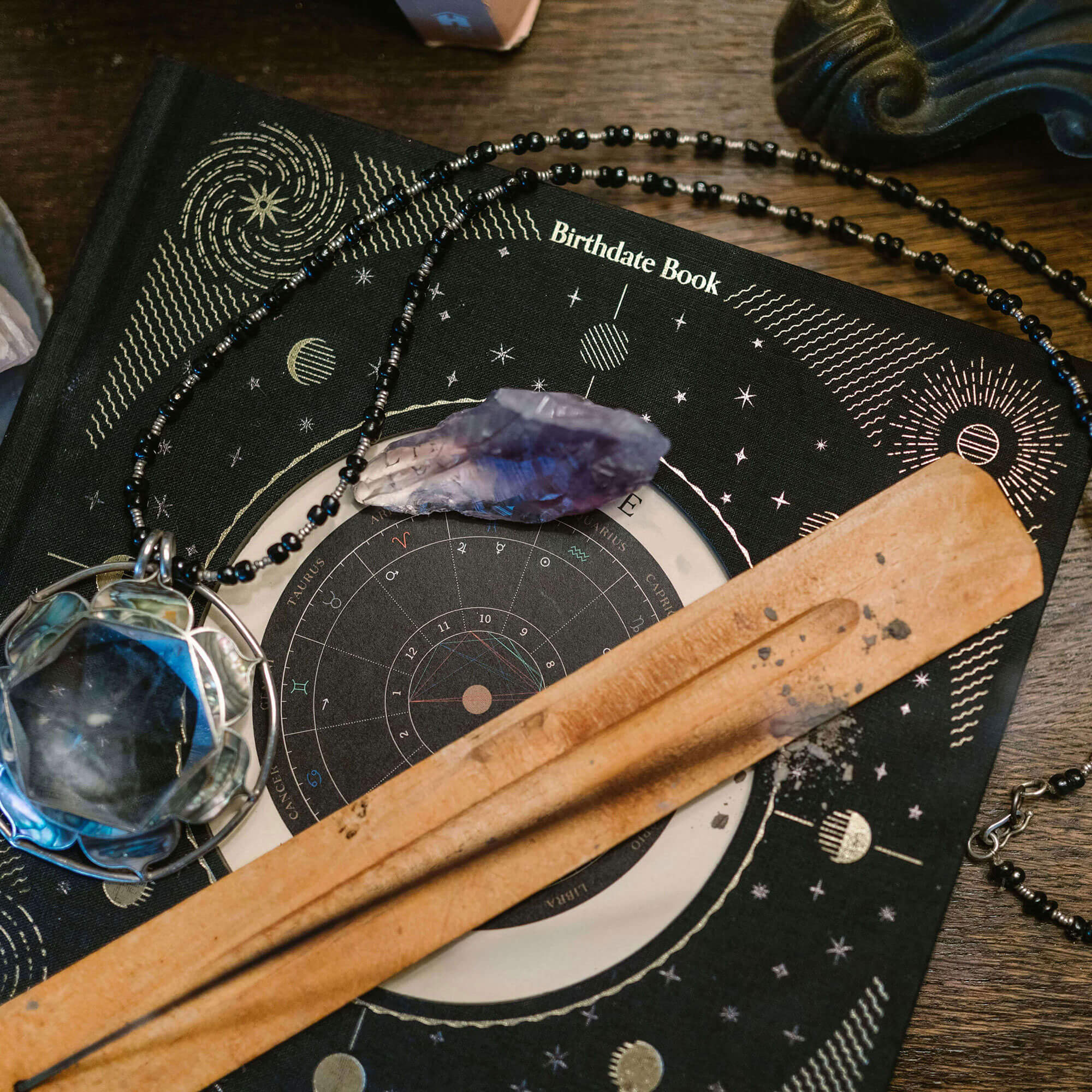 Astrological book with crystal, necklace, and wooden tool on a wooden surface