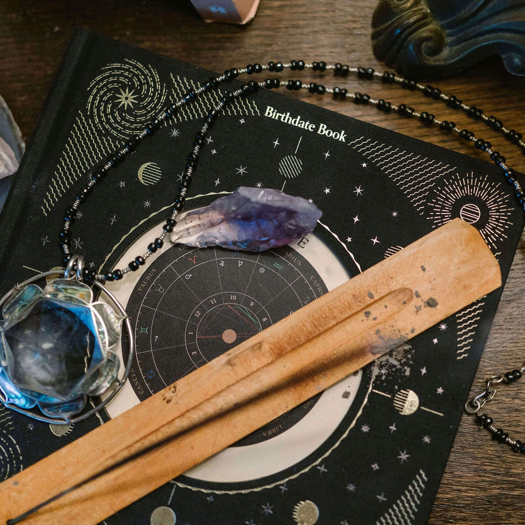 Astrological book with crystal, necklace, and wooden tool on a wooden surface