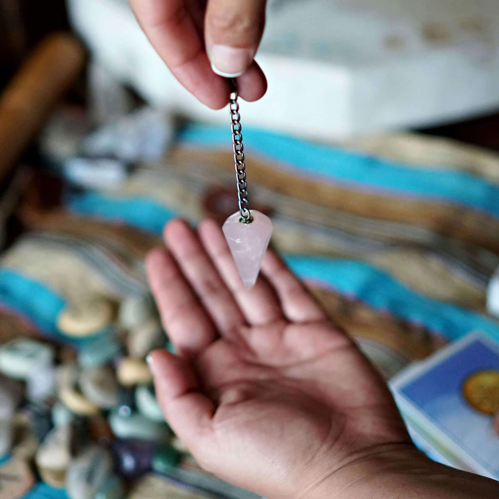 Person holding a pink crystal pendulum over their palm with a blurred background