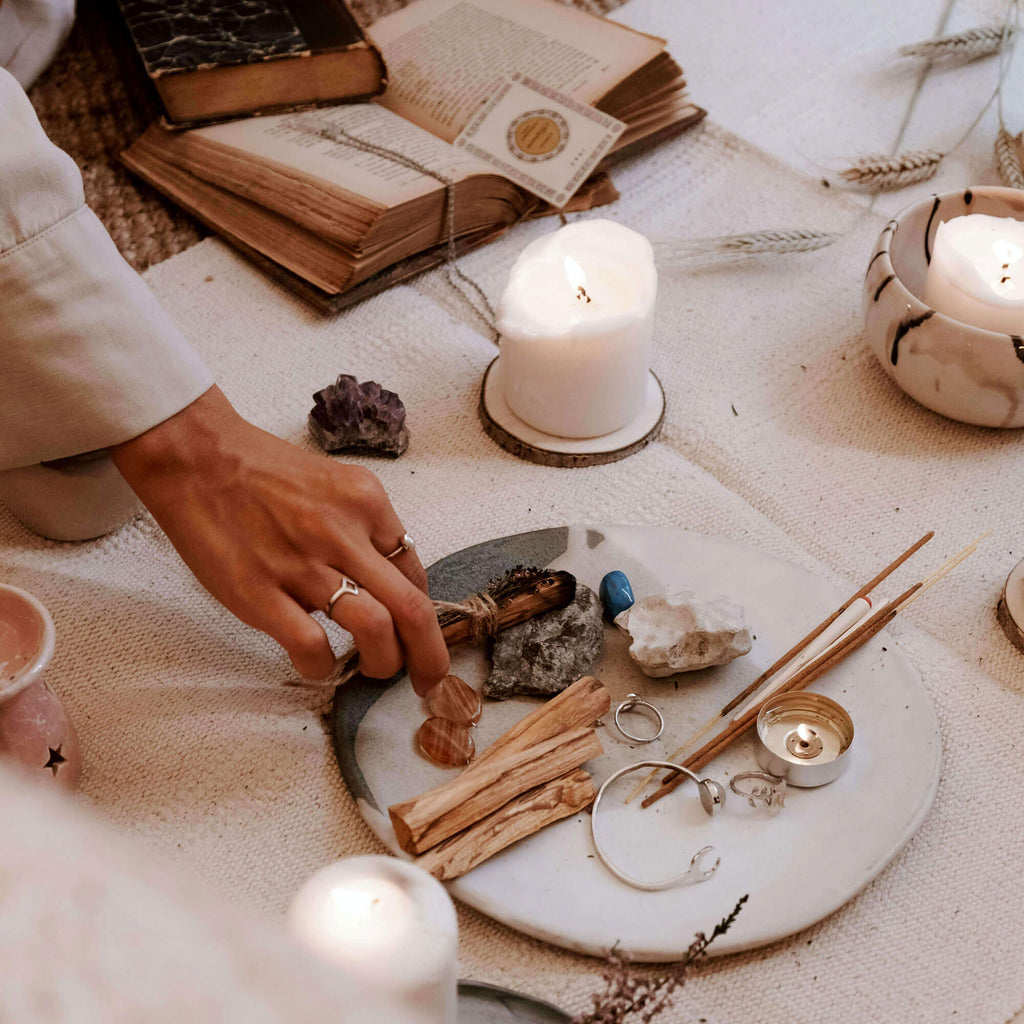 Person interacting with objects on a table including books, candles, and natural elements.