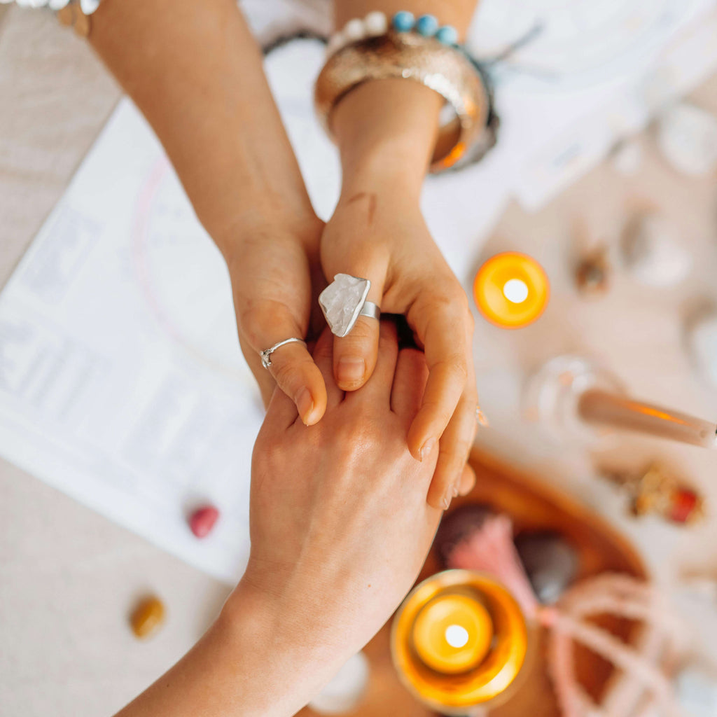 Two hands holding each other with a blurred background of candles and flowers