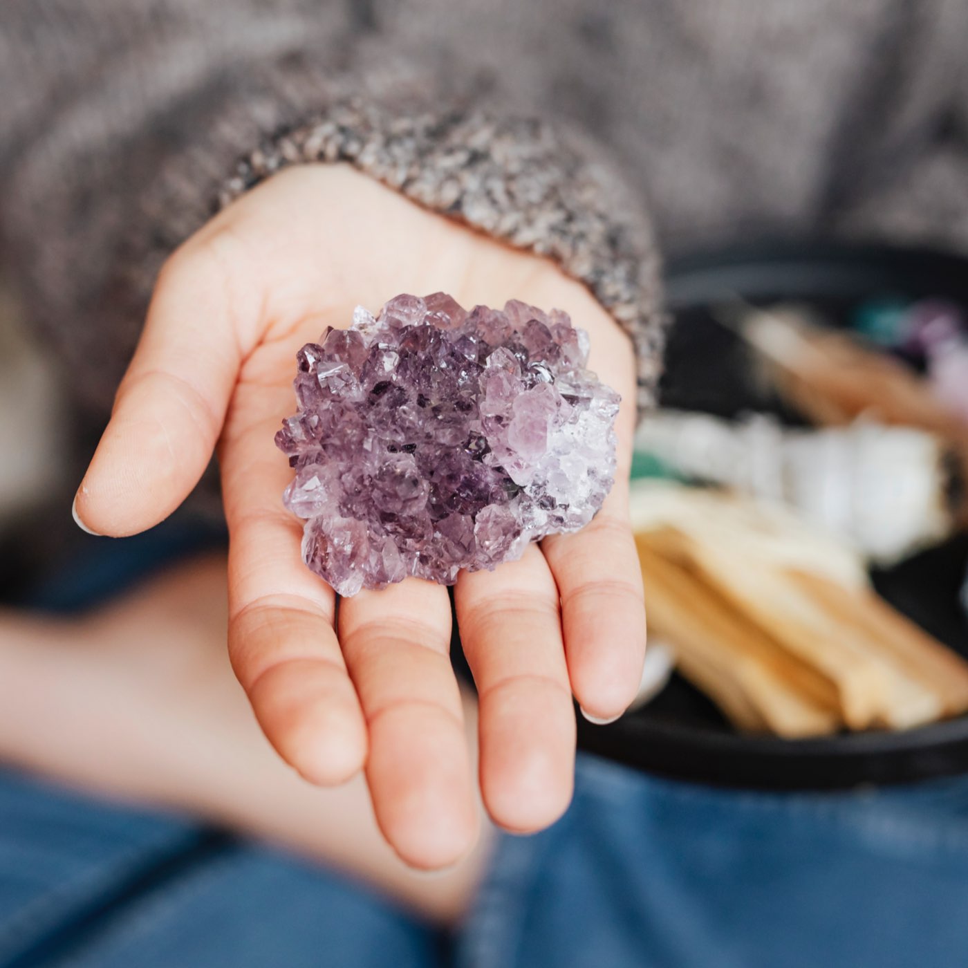 A person holding a purple crystal in their hand, with various spiritual items displayed in the background.